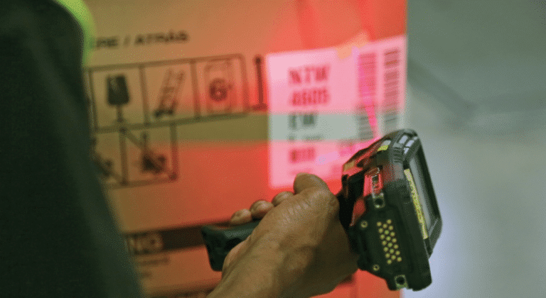 Close-up of a warehouse worker scanning a barcode on a cardboard box with a handheld scanner.
